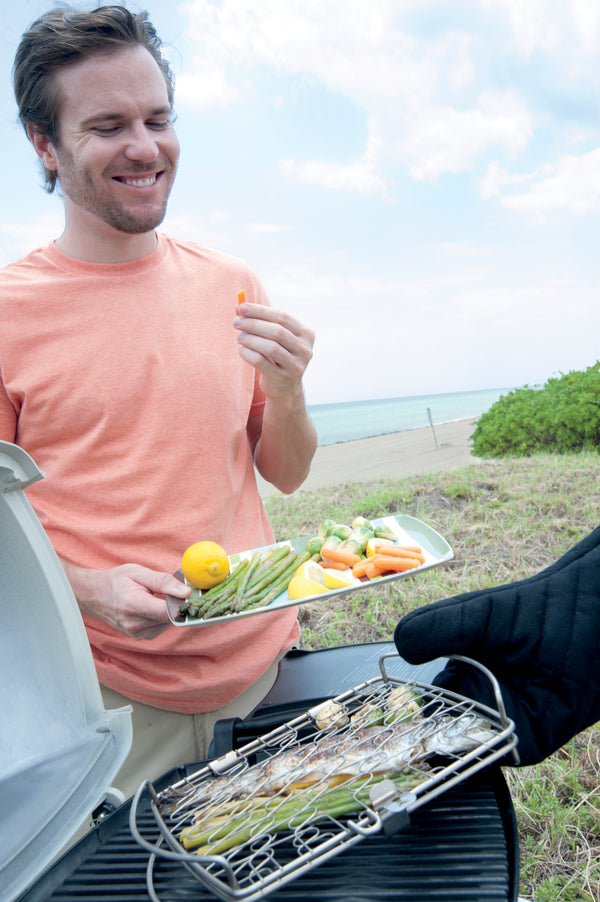 Persona en playa comiendo verduras asadas utilizando la canasta de acero inoxidable  para asar sobre la parrilla
